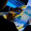 Two businesspeople analyze charts and graphs over a desk with a laptop in the background.