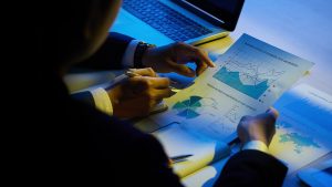 Two businesspeople analyze charts and graphs over a desk with a laptop in the background.