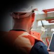Construction worker in a hard hat and orange safety vest uses a tablet with a checklist at an active building site.