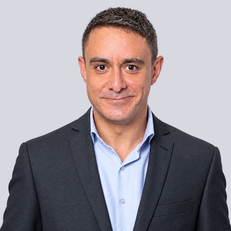 Professional headshot of a smiling man in a dark blazer and light blue shirt.